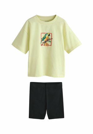 Yellow short-sleeve t-shirt featuring a colorful bird graphic within a square, paired with black fitted shorts. Both made of soft fabric.
