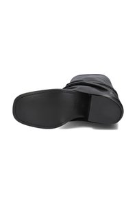 Zwarte leren laars met een glad bovenwerk, slouchy ontwerp, ronde neus en platte rubberen zool. Minimale stikdetails zichtbaar.