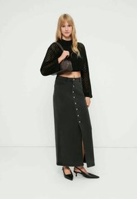 Svart kort stickad tröja med vida ärmar, kombinerad med en lång grå jeanskjol med framslits och silverknappar. Svarta klackar.