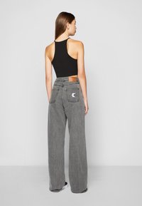 Svart avskåret tanktopp kombinert med høytlivs, vide gråjeans. Jeansene har et brunt lærmerke og to baklommer med detaljer.