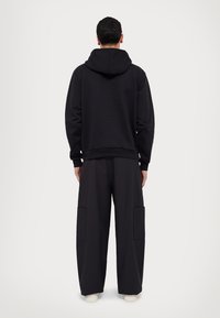 Czarna bluza z kapturem na sznurki i ściągaczami przy mankietach, zestawiona z szerokimi czarnymi spodniami z dwoma bocznymi kieszeniami. Prosty, minimalistyczny design.