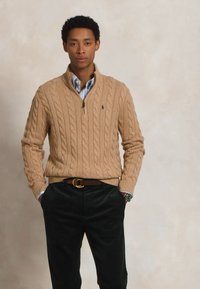 Suéter bege com malha canelada e fecho de zíper de um quarto, combinado com uma camisa azul clara de colarinho e calças verdes escuras, criando um visual em camadas.