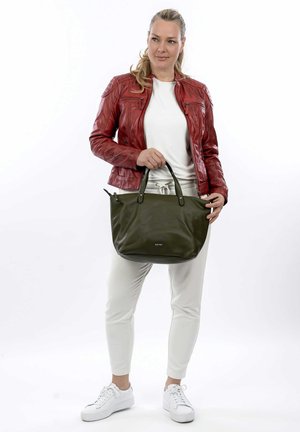Borsa tote in pelle verde oliva con due manici superiori, superficie texturizzata e un logo discreto. Indossata con una giacca di pelle rossa e sneakers bianche.