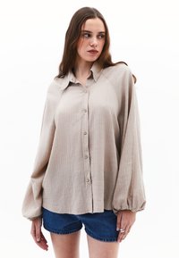 Camicia button-up beige chiaro con un tessuto testurizzato, vestibilità comoda e maniche a palloncino, abbinata a pantaloni corti in denim.