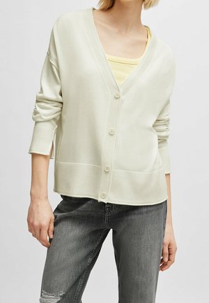 Ljust grön cardigan med V-hals, ribbade ärmslut och nederkant, samt knäppning fram. Bärs över en gul topp med avslappnad passform och mjuk textur.