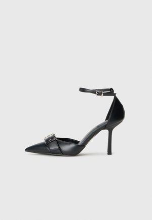 Escarpin noir en cuir avec un bout pointu, une bride à la cheville et un accent de boucle en argent. Texture lisse avec une silhouette élégante.