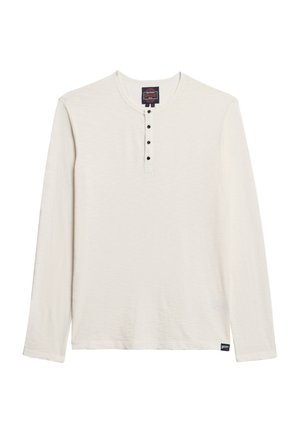 Camisa henley de manga larga en crema con una tela texturizada, que presenta un cuello redondo y cinco botones negros en la parte delantera.