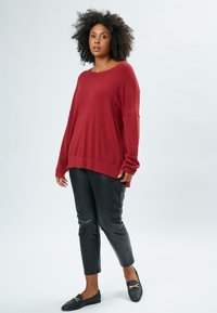 Rotem übergroßes Sweatshirt mit langen Ärmeln, kombiniert mit schwarzen, taillierten Hose aus Kunstleder und schwarzen Slippern. Schlichtes Design, weicher Stoff.