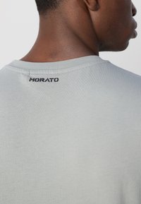 Vaaleanharmaa t-paita pyöreällä kaula-aukolla, jossa musta "MORATO" -logo takakaulan kohdalla. Sileä pinta ja normaali istuvuus.