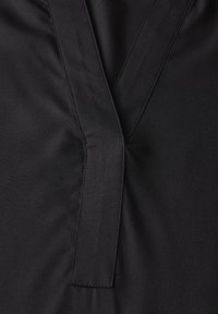 Tessuto nero con design a V e una cucitura centrale, caratterizzato da una leggera texture. Linee pulite e dettagli di cucitura minimal.