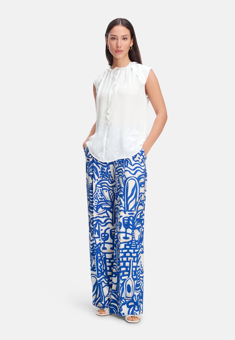 White sleeveless blouse with ruffled neckline, paired with blue and white patterned wide-leg pants featuring abstract designs.