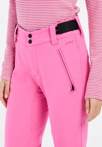 Roze skibroek van flexibel materiaal, met een ritszak, dubbele knoopsluiting en een zwarte riem met strepen.
