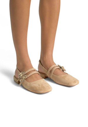 Ballerines en suède beige avec un bout carré, ornées de deux brides décoratives et d'un accent bijou sur le côté. Talon bas et plat. Texture lisse.