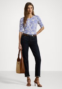 Top floreale blu e bianco, jeans scuri slim-fit, borsa marrone e sandali alti color beige. Design semplice e casual.