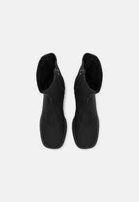 Bottines noires avec une texture lisse et élégante, dotées d'une fermeture éclair sur le côté et d'une forme cintrée, conçues pour un maintien ajusté.