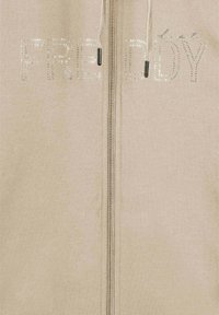 Felpa beige con zip e la scritta "FREDDY" in strass argento. Presenta una zip frontale e un cappuccio regolabile con coulisse. Tessuto morbido e liscio.