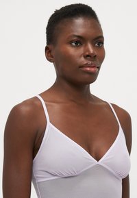 Bralette bianco in morbido tessuto con spalline sottili, caratterizzato da un design a V e dettagli arricciati al centro. Texture liscia e finitura delicata.