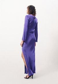Lila Satin-Kleid mit langen Ärmeln, hohem Schlitzausschnitt und Schlüsselbeingröße auf der Rückseite; glatte Textur und figurbetonter Schnitt.