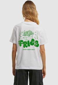 Witte katoenen t-shirt met een groene afbeelding van frietjes in een verpakking en de tekst "FRIES" en daaronder "CRISP VIBES ONLY".