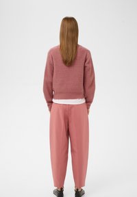 Kort, lyserød striktrøje med struktureret stof og cropped design. Parret med løstsiddende, højtaljede lyserøde bukser og sorte sko.