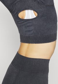 Schwarzes Sport-Crop-Top mit geripptem unteren Bund und Ausschnitt-Detail, kombiniert mit passenden hoch taillierten Leggings. Glatte Textur, körperbetontes Design.