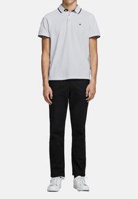 Lichtgrijze polo met zwarte afwerking op de kraag en mouwen, gecombineerd met zwarte broek en witte sneakers. Gladde textuur, klassieke pasvorm.