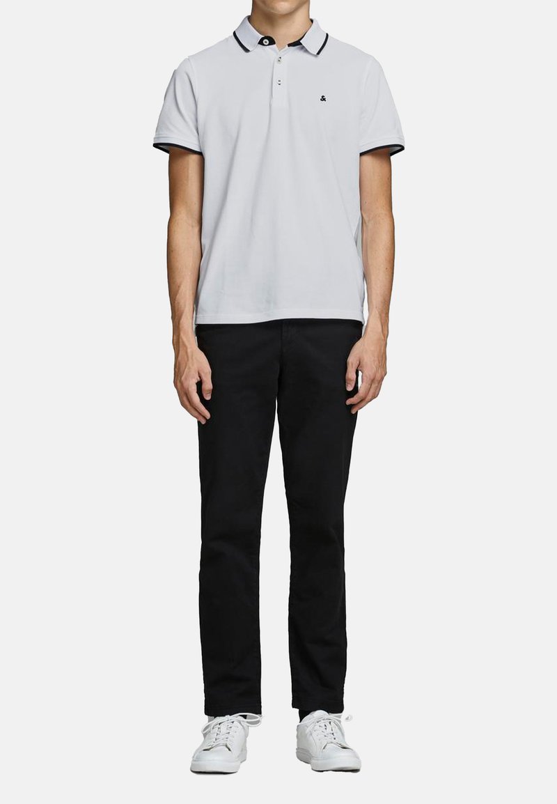 Lichtgrijze polo met zwarte afwerking op de kraag en mouwen, gecombineerd met zwarte broek en witte sneakers. Gladde textuur, klassieke pasvorm.