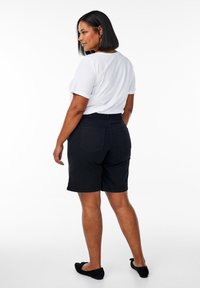 Pantalones cortos de mezclilla negros con cintura alta, bolsillos traseros y un ajuste entallado. Combinados con una camiseta blanca de corte holgado y zapatos planos negros.