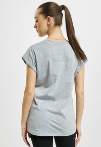 T-shirt grigia a maniche corte con una vestibilità rilassata, scollo a costine e texture morbida, vista da dietro, abbinata a pantaloni neri.