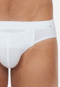 Slip bianchi da uomo realizzati in tessuto morbido con una cintura liscia. Presentano una tasca frontale e dettagli di cucitura minimi.