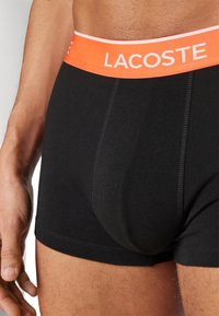 Svarta bomullskalsonger med ett orange elastiskt midjeband och vitt logotyp. Har en figurnära design och slät textur.