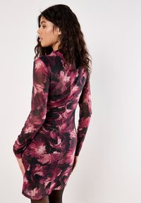 Blumendruckkleid in Schattierungen von Pink und Schwarz, mit figurbetontem Design, langen Ärmeln und einem gerafften Rücken für zusätzliche Textur.