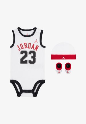 Combinaison en coton blanche avec des bordures noires, présentant "JORDAN" et "23" en rouge et noir, accompagnée d'un chapeau blanc avec une bande rouge et de chaussons assortis.