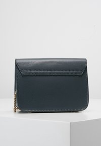 Grå texturerad läderhandväska med klaffstängning, kedjedetalj på sidan och rektangulär form. Kompakt design för enkel bärbarhet.