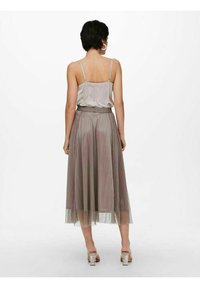 Gonna midi plissettata in grigio chiaro con vita sottile, abbinata a una canotta in satin. La gonna presenta un tessuto trasparente e fluido.
