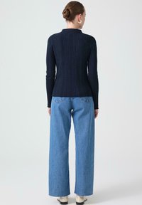 Marineblå ribbad tröja med långa ärmar, figurnära siluett och hög krage, i kombination med vida blå denimjeans med fransad fåll.