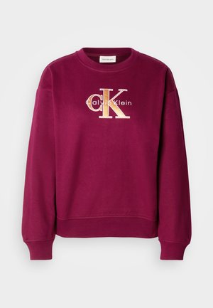 Bordo majica s crew izrezom i dolgimi rokavi. Vezen zlati logo "CK" s tekstom "Calvin Klein" spodaj. Mehka tkanina.
