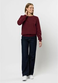 Felpa bordeaux con scollo rotondo, polsini e orlo a coste; abbinata a jeans a gamba larga blu scuro e sneakers bianche.
