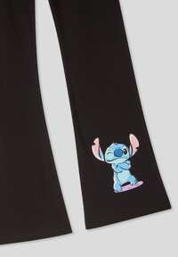 Pantaloni neri con una grafica colorata di un personaggio cartoon blu con grandi orecchie e braccia incrociate, posizionata sulla parte inferiore della gamba sinistra.