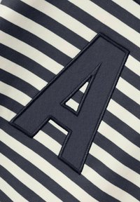 Letra "A" bordada en negro sobre un fondo de tela de rayas horizontales en blanco y azul marino.