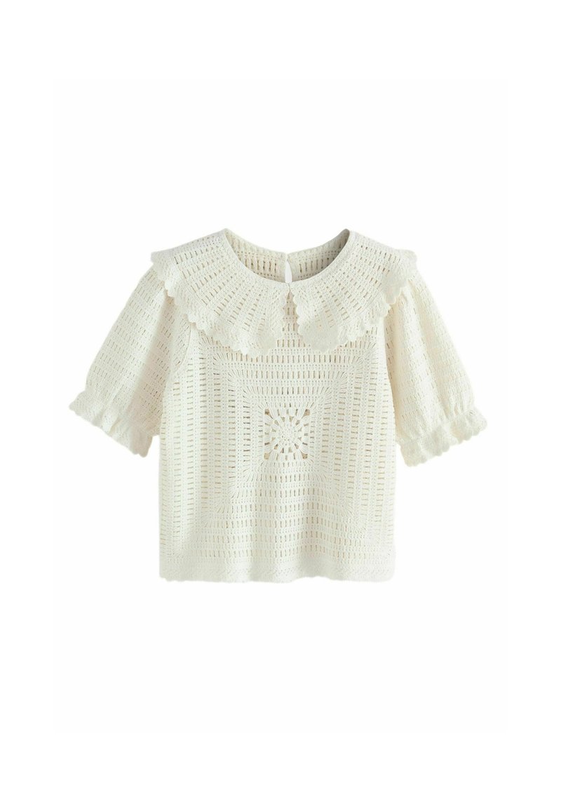 Haut en crochet blanc avec col Peter Pan festonné et manches courtes bouffantes ornées de bords froncés.
