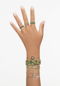 Drei Ringe mit grünen und rosa Steinen sowie mehrere Armbänder mit goldenen Akzenten, grünen Edelsteinen und einem Schmetterlingsdesign auf einem Armband.