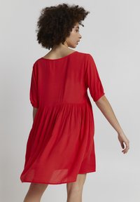 Robe rouge à manches courtes avec une coupe décontractée, dotée d'une taille froncée, d'un tissu fluide et d'un dos en scoop. Texture lisse.