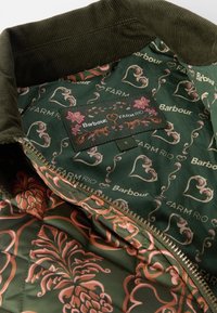 Interior de uma jaqueta verde acolchoada com padrões florais e de corações em rosa e laranja, apresentando etiquetas de logotipo da Barbour e FARM RIO. Colarinho de veludo corduroy.