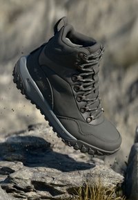 Bota de caminhada impermeável cinza com sola de borracha, ilhós de metal e parte superior texturizada. Colarinho acolchoado e saliências de tração para estabilidade em terrenos irregulares.