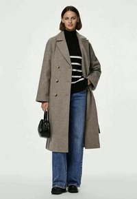 Divrindis pelēks vilnas mētelis ar lieliem pogām, uzvilkts virs melnā svītrainā turtleneck, apvienots ar platajiem zilo džinsu biksēm un melnām kurpēm.