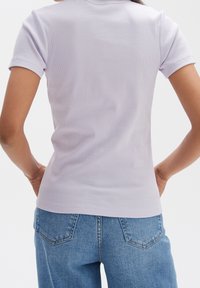Lilac ribbed polo shirt with a fitted silhouette and short sleeves, paired with light blue high-waisted denim jeans featuring back pockets.