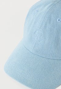 Ανοιχτό μπλε τζιν καπέλο μπέιζμπολ με καμπυλωτό γείσο και μικρό ανάγλυφο κυκλικό σχέδιο λουλουδιού στο μπροστινό πάνελ.