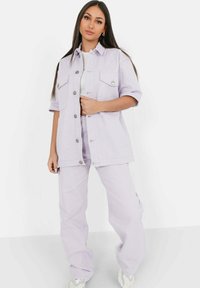 Lilafärgad denimjacka med två bröstfickor, knäppning med knappar och korta ärmar, matchad med lilafärgade raka byxor.