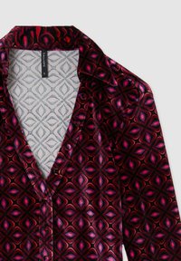 Blusa rossa e nera con motivo a fantasia, con scollatura a V, caratterizzata da motivi floreali e una texture setosa. Contiene un'etichetta con la scritta "CALLIOPE" taglia S.